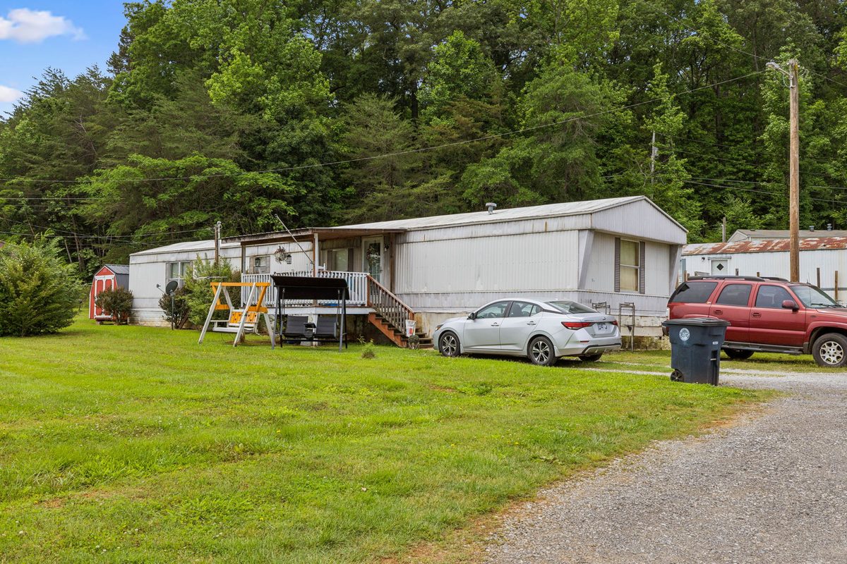 Park-owned home with wooden deck, playset, and resident parking